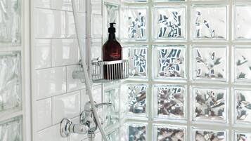 Ein Badezimmer mit einer Duschkabine aus Glas, einer Handbrause und einer Shampooflasche auf einem Regal.