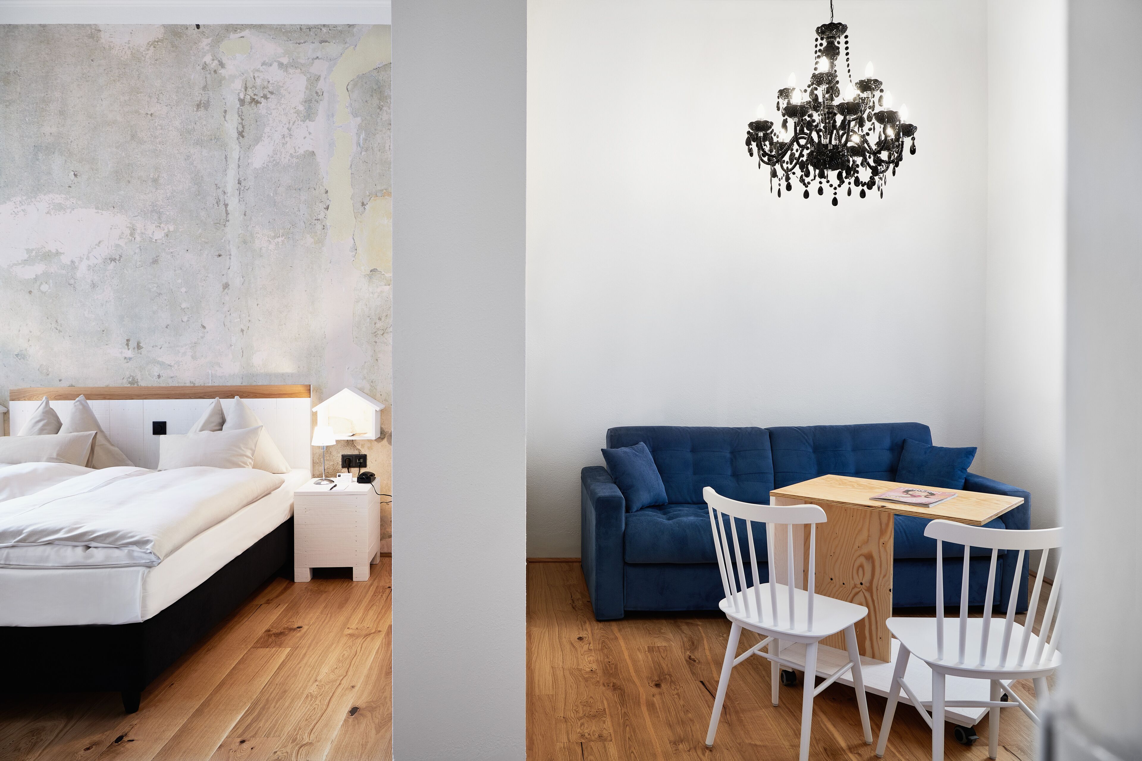 A bedroom with a bed, bedside table, and lamp, and a living area with a sofa, chairs, and a table.