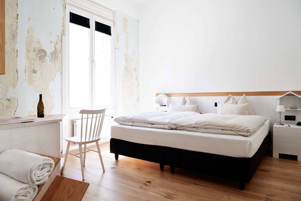 A bedroom with a bed, a chair, a nightstand, and a window with curtains.