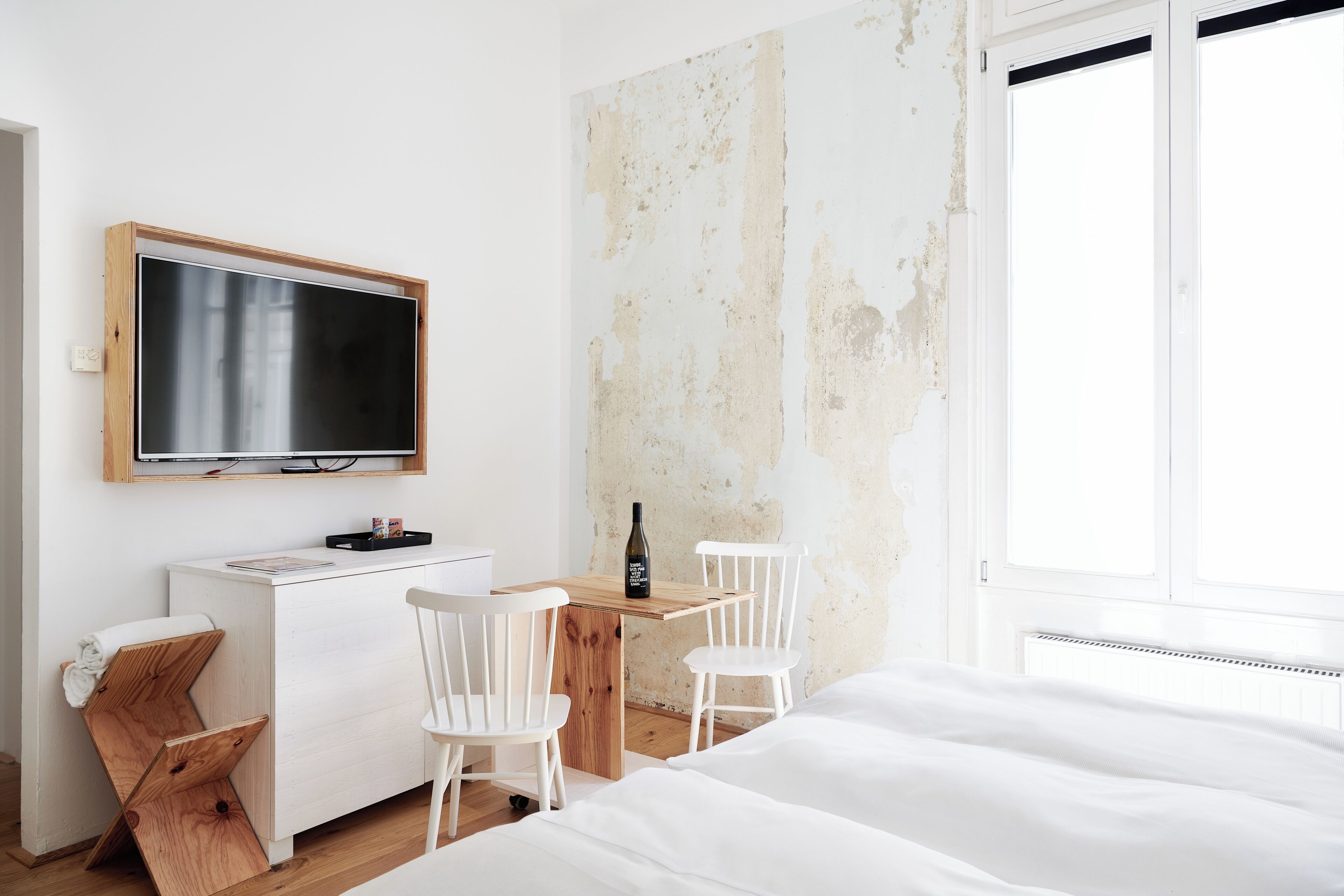 Ein schlicht eingerichteter Raum mit einem Bett, einem Schreibtisch, zwei Stühlen, einem Fernseher und einem Fenster.