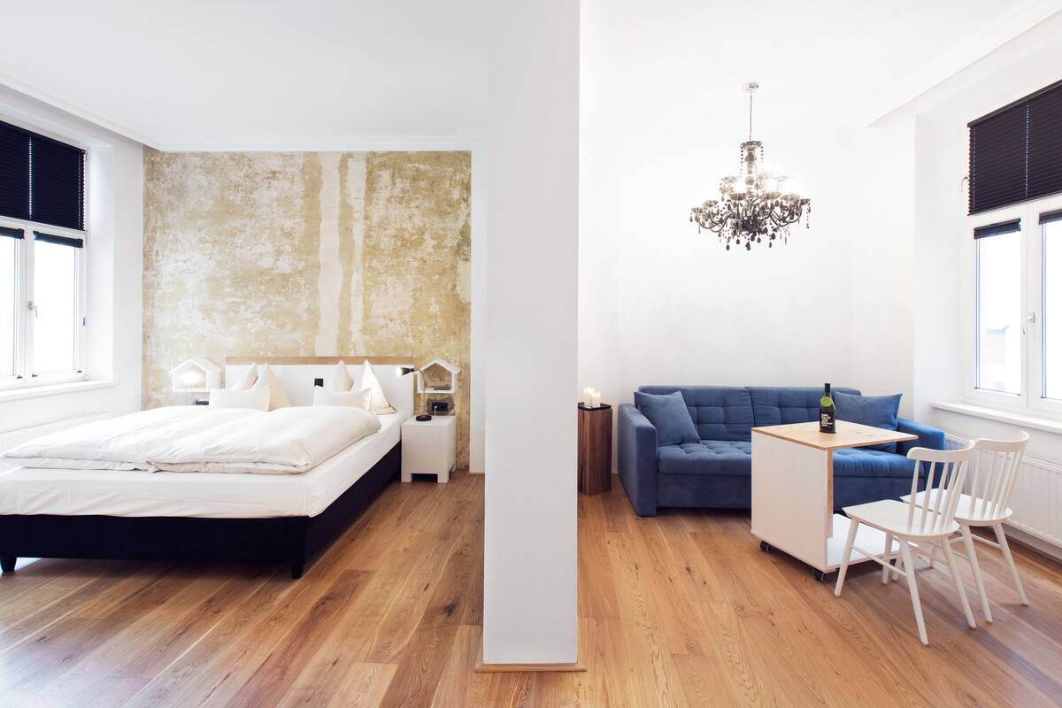 A modern bedroom with a large bed, a blue sofa, a small table with a bottle, and a chandelier.