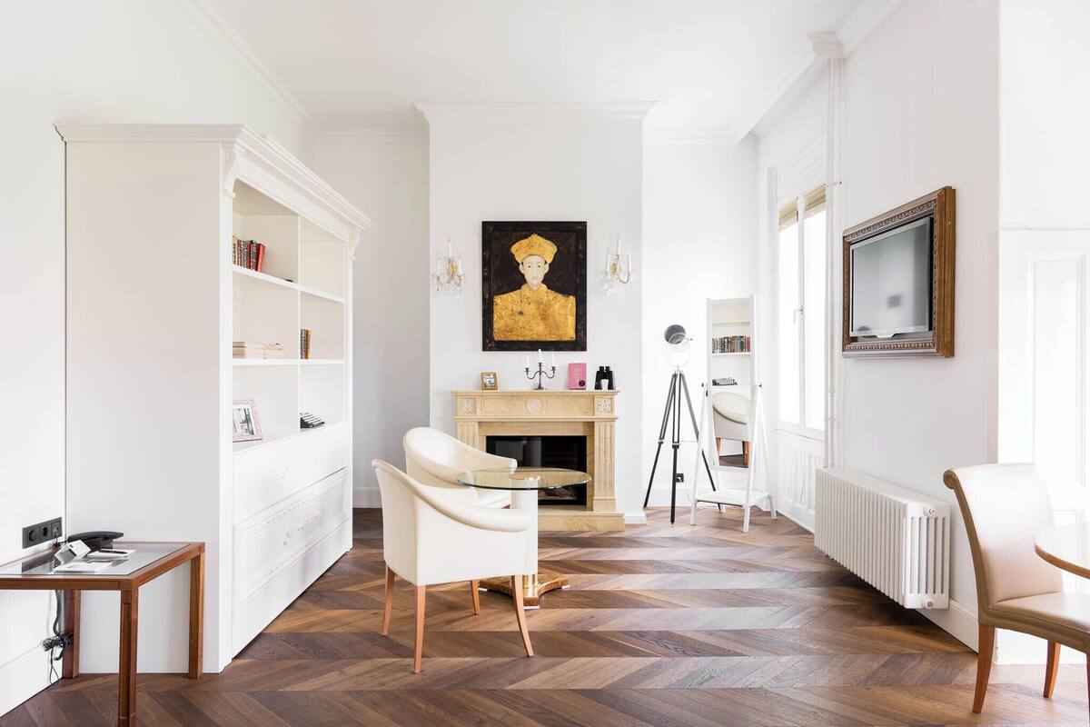 A room with a fireplace, white walls, a wooden floor, and a white chair.