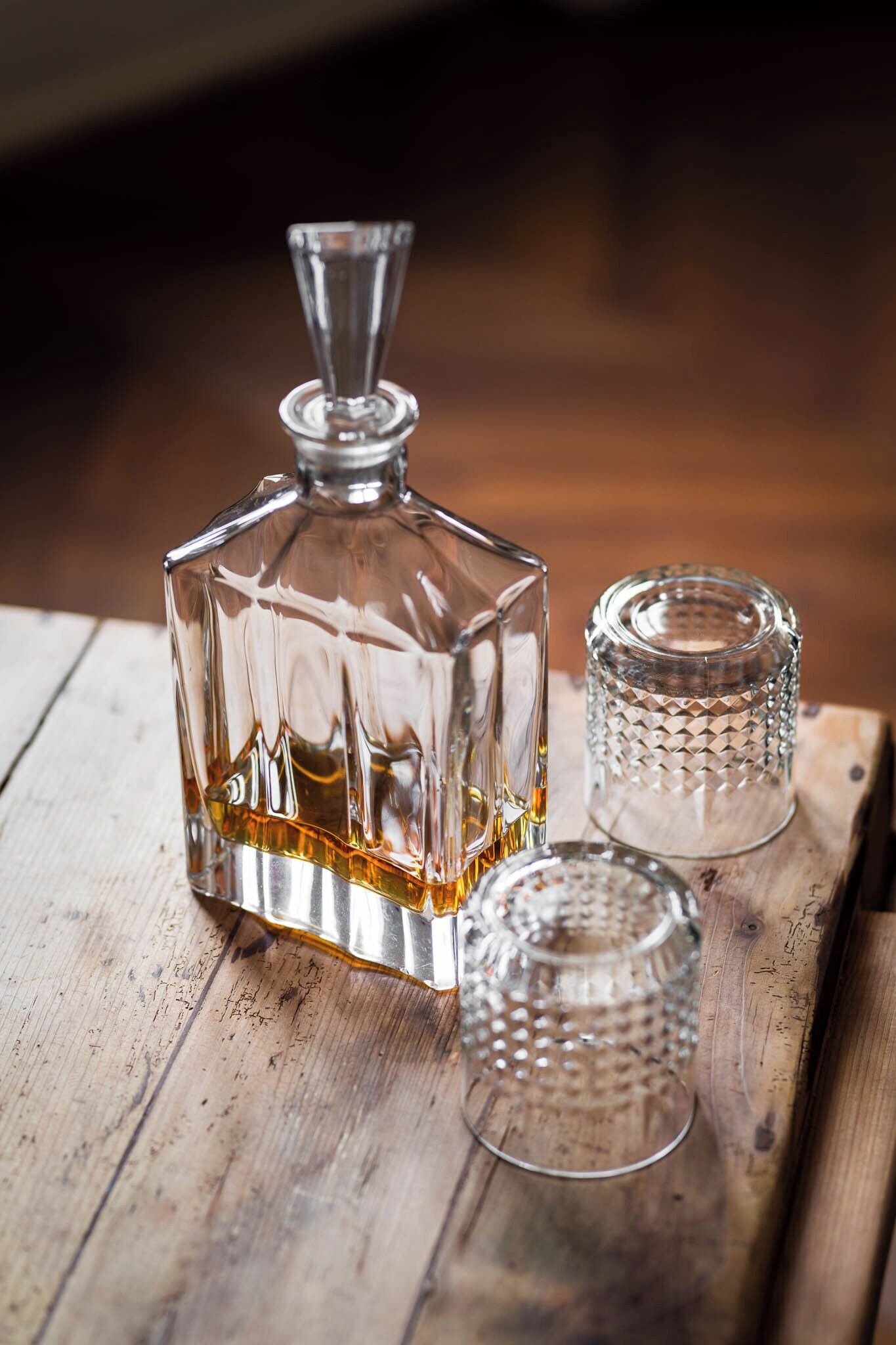 A clear glass decanter and two glass tumblers on a wooden surface.