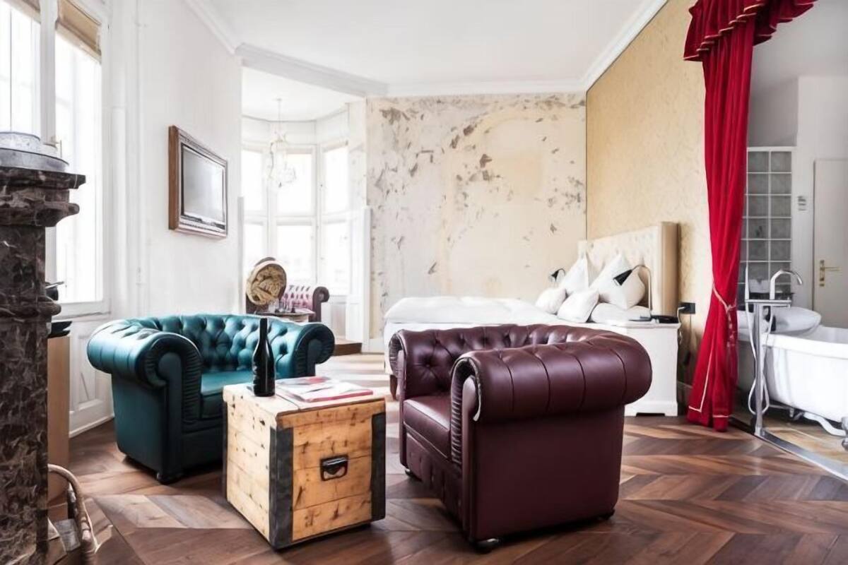 A room with a bed, two sofas, a wooden chest, and a stone fireplace.