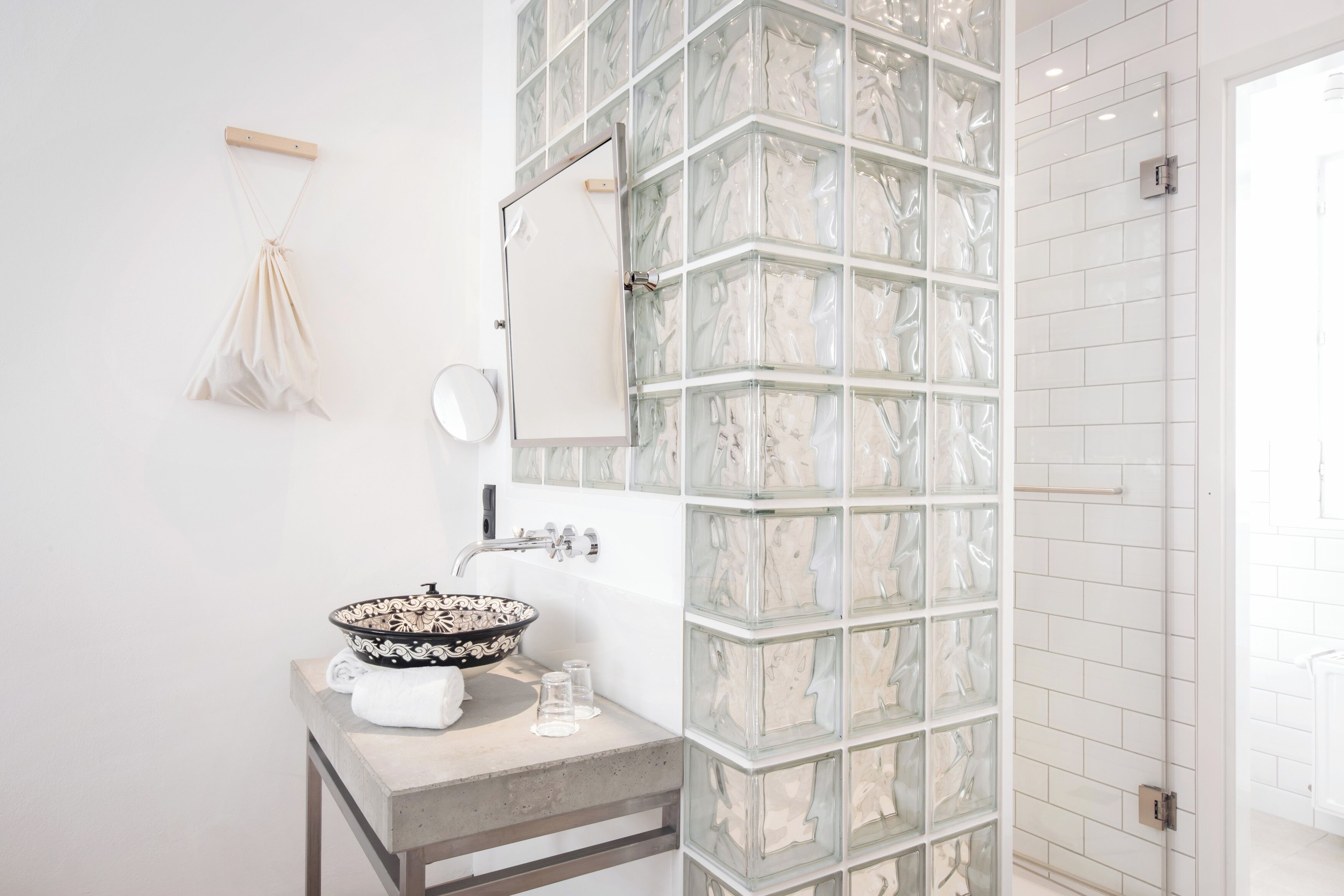 A bathroom with a glass block shower enclosure, a white sink with a decorative bowl, and a towel rack.