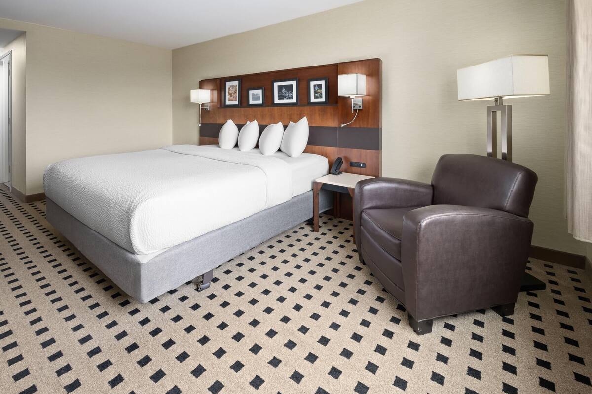 A hotel room with a large bed, a desk with a lamp, and a leather armchair.