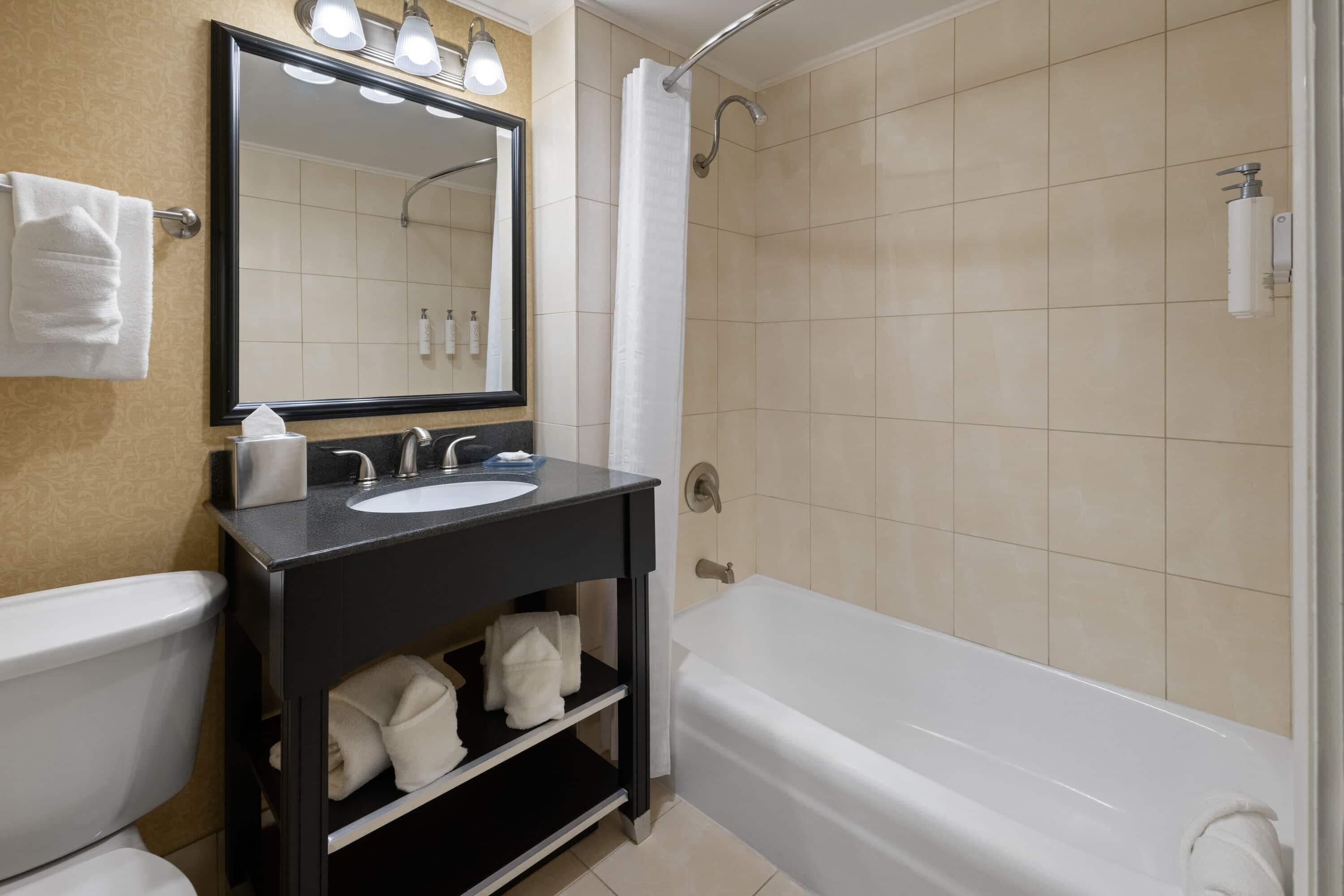 A bathroom with a toilet, sink, mirror, and bathtub.