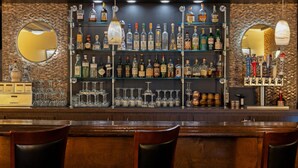 Eine Bar mit mehreren Regalen voller Spirituosenflaschen, Gläsern und einer Theke mit Stühlen.