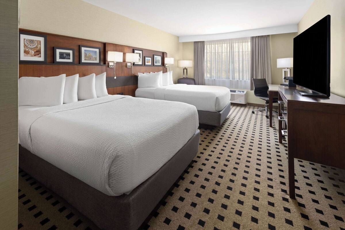 A hotel room with two beds, a desk, a television, and a patterned carpet.