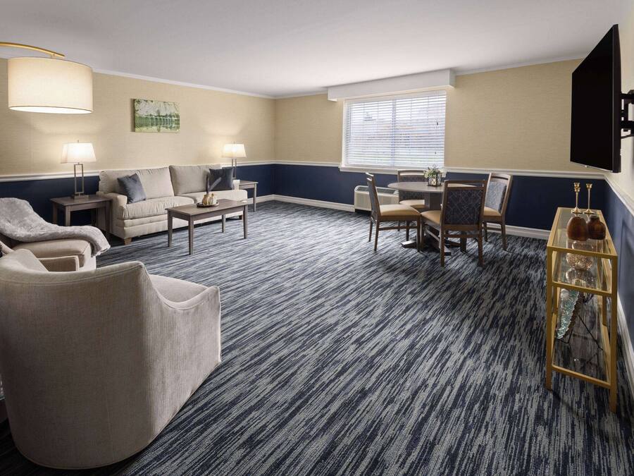 A hotel room with a large window, a sofa, a chair, a small table, and a lamp.