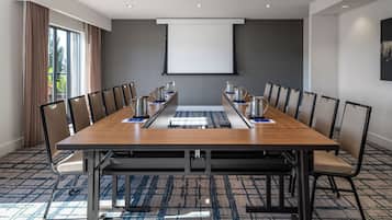 A conference room with a long table, chairs, a projector screen, and a carpeted floor.