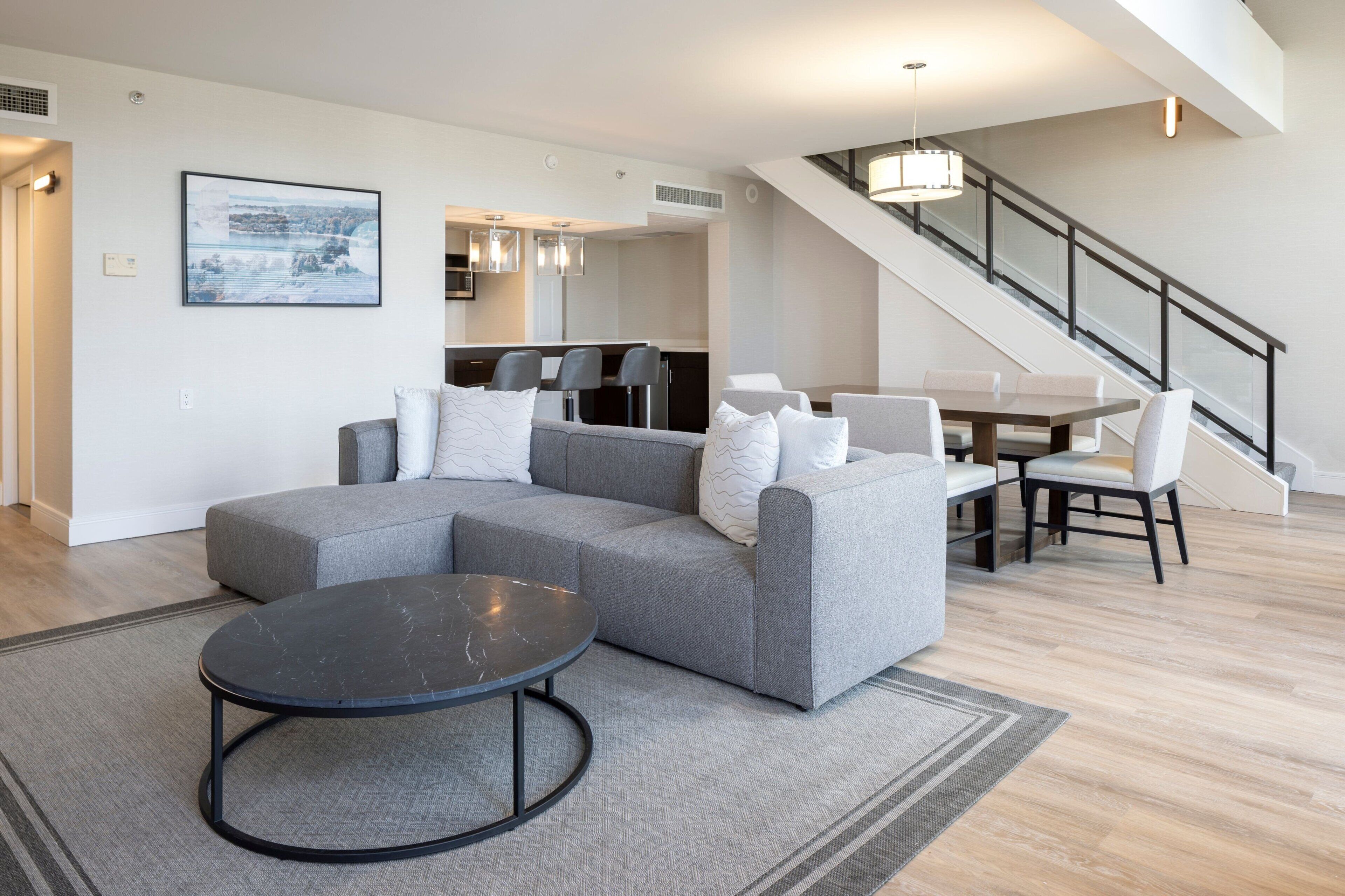 A modern living room with a sectional sofa, a dining table with chairs, and a staircase leading to an upper level.
