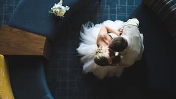 A couple embracing in a room with a blue patterned floor, a wooden side table, and a small white flower arrangement.