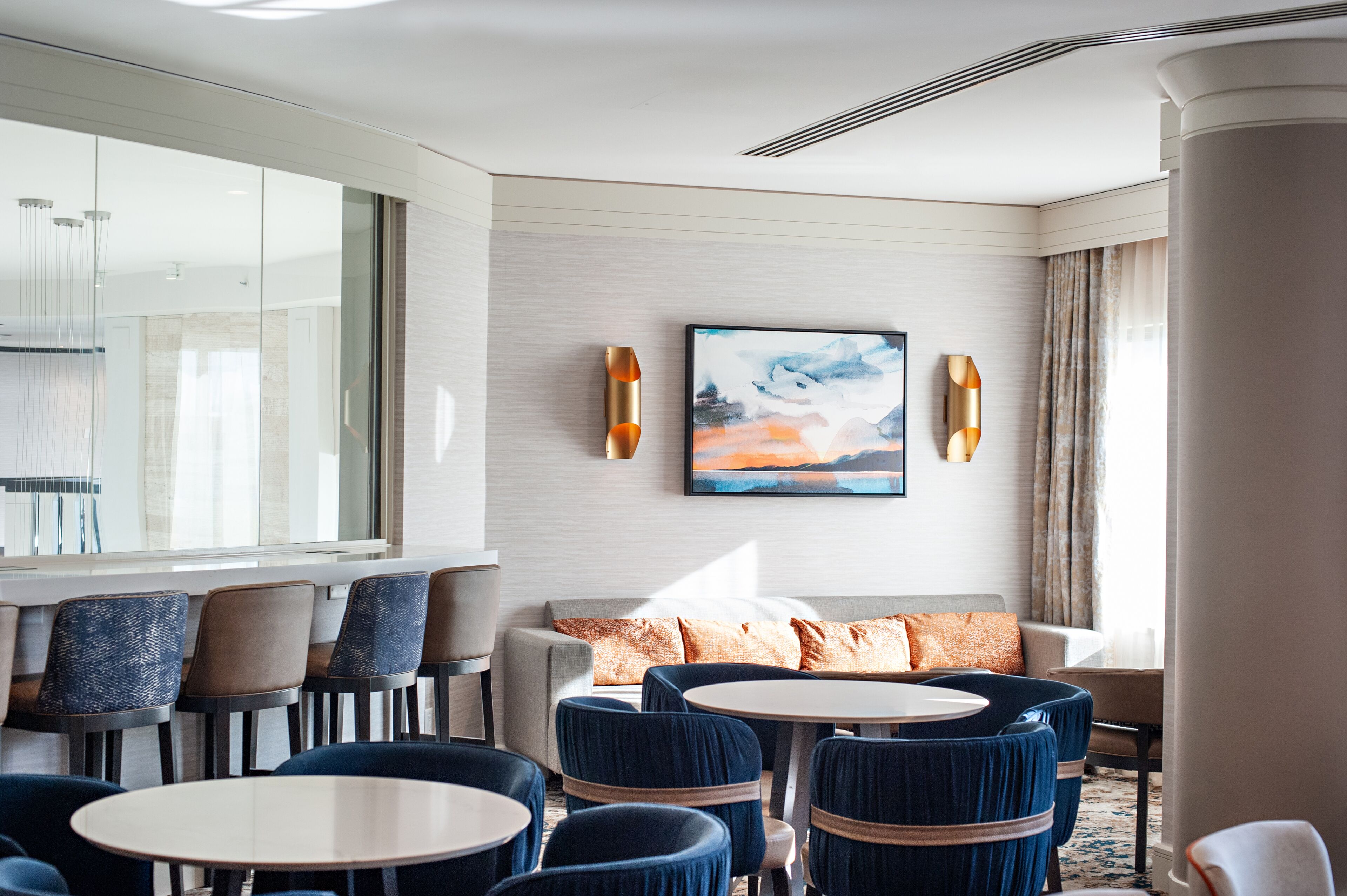 A modern hotel lobby with a seating area, a large window, and a painting on the wall.
