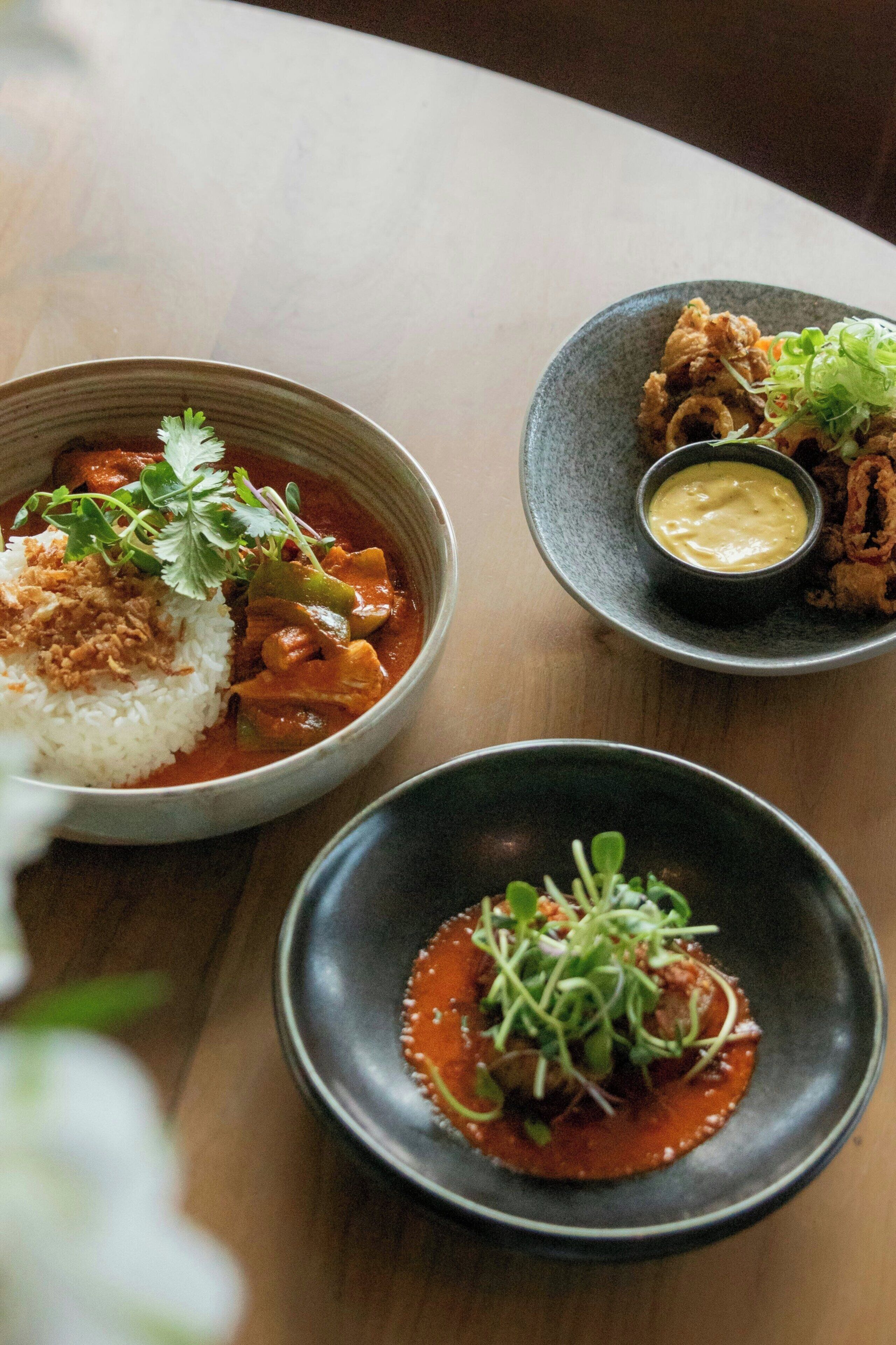 A table with three bowls of food, each with different sauces and garnishes.