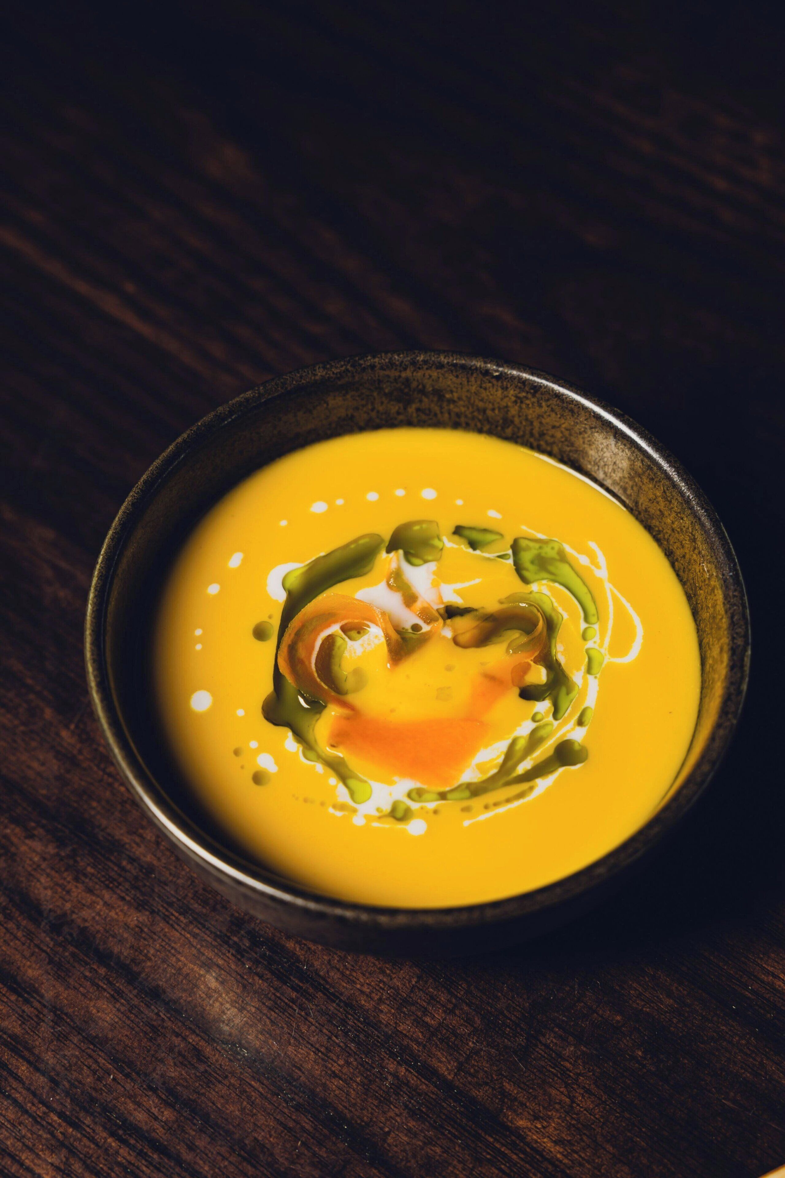 Eine Schüssel Suppe mit einem grünen Soßenwirbel auf einem dunklen Holztisch.