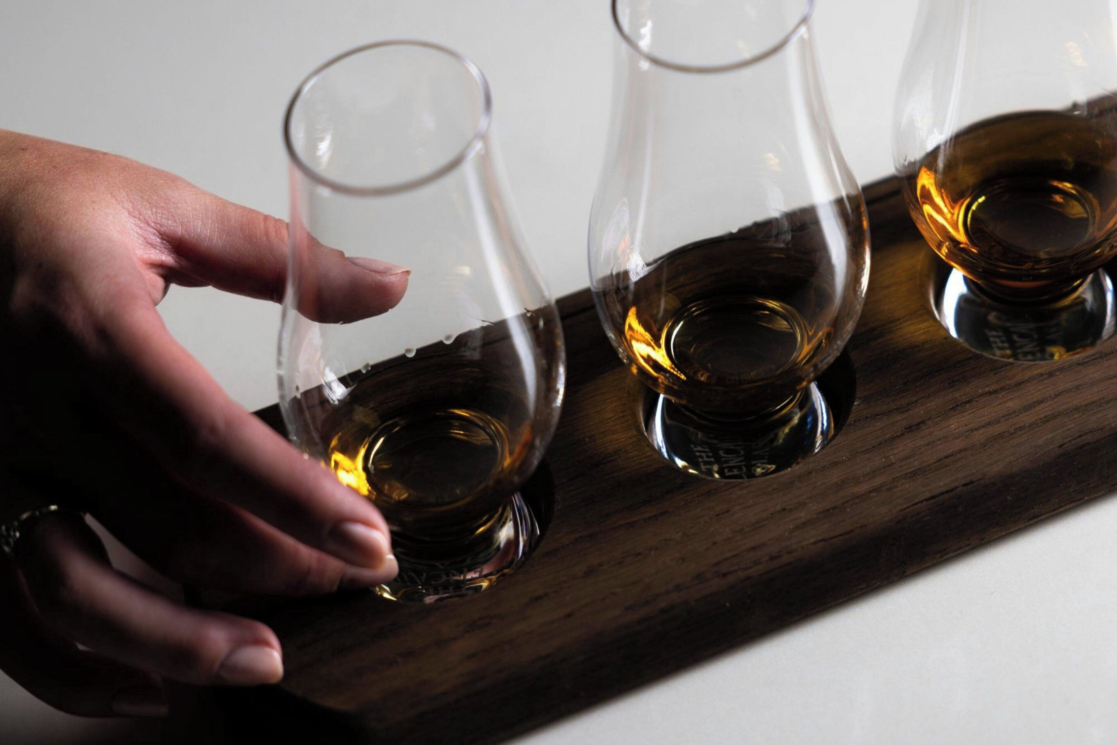 Eine Hand hält ein Glas auf einem hölzernen Tablett mit drei Gläsern.