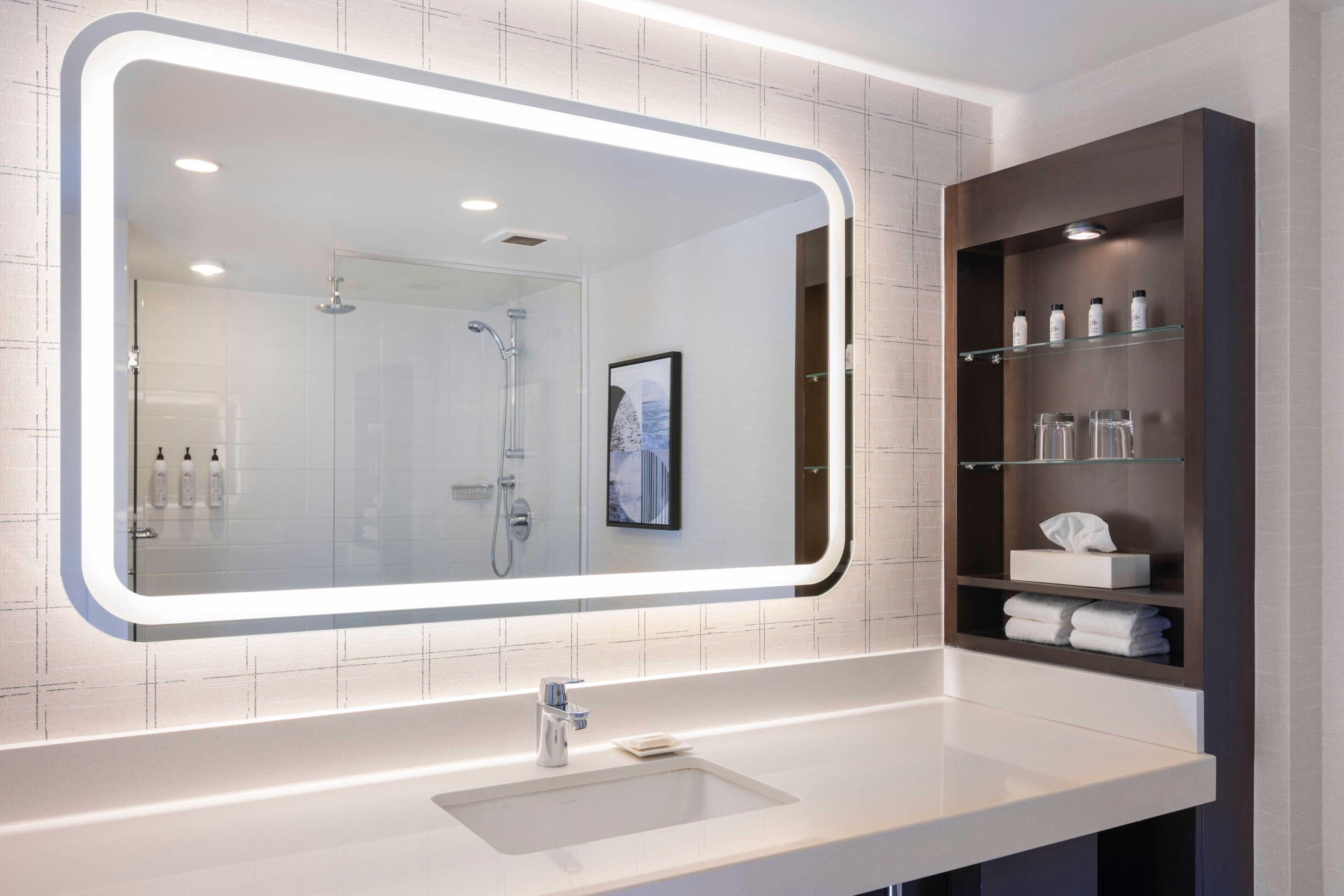 A modern bathroom with a large mirror, a sink, and a shelf with toiletries.