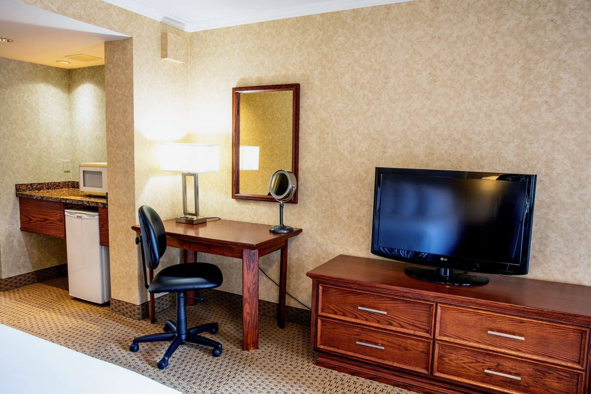 Una habitación de hotel con un escritorio de madera, televisor, silla, refrigerador pequeño y espejo.
