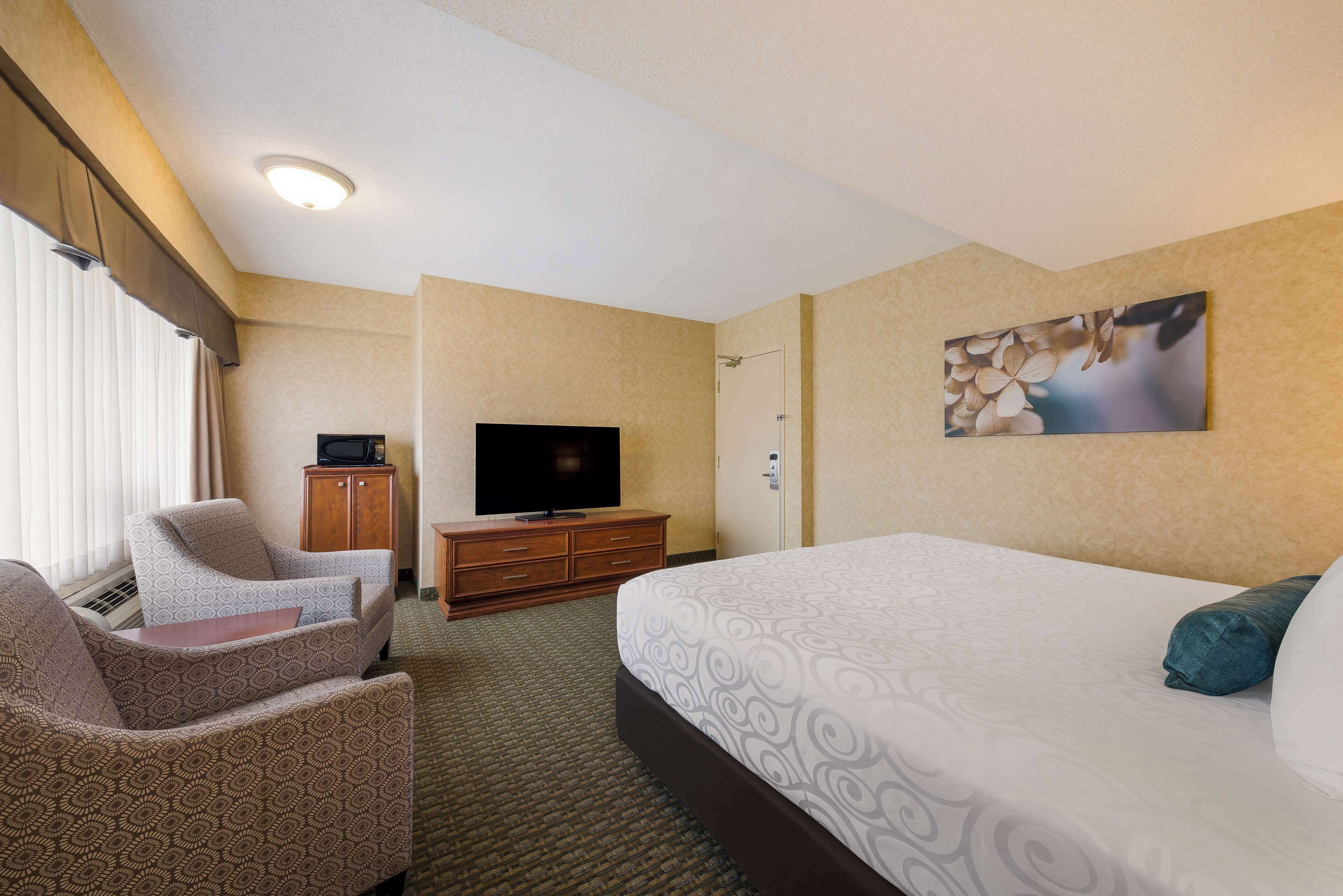 Habitación de hotel con cama, televisión, zona de estar y un cuadro en la pared.