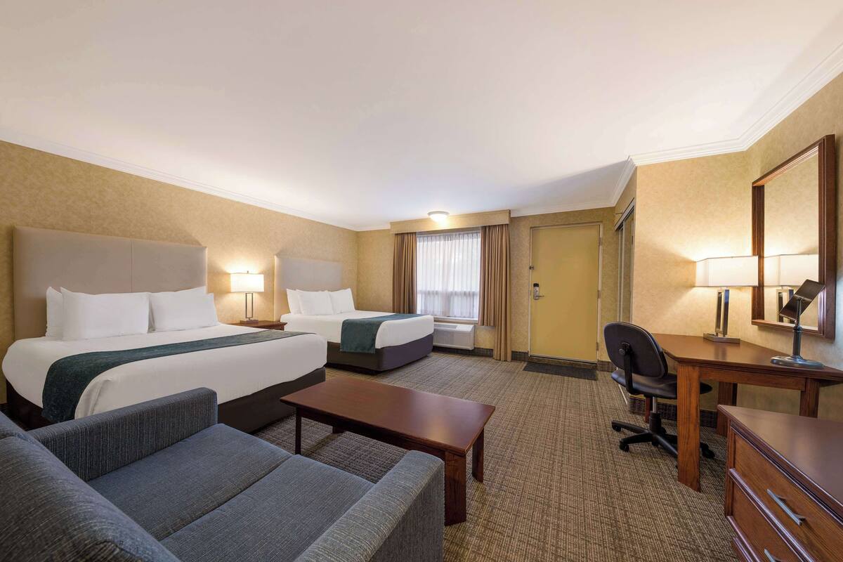 Una habitación de hotel con una cama grande, dos camas individuales, un escritorio, una silla, un sofá y un aparador.