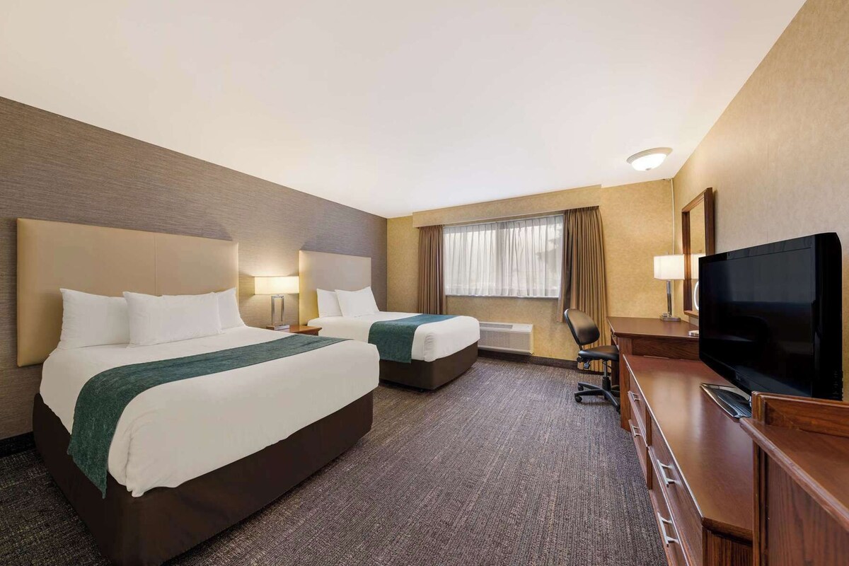 A hotel room with two beds, a TV, a desk, and a window with curtains.
