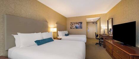 A hotel room with two beds, a desk, a TV, and a bathroom visible through an open door.