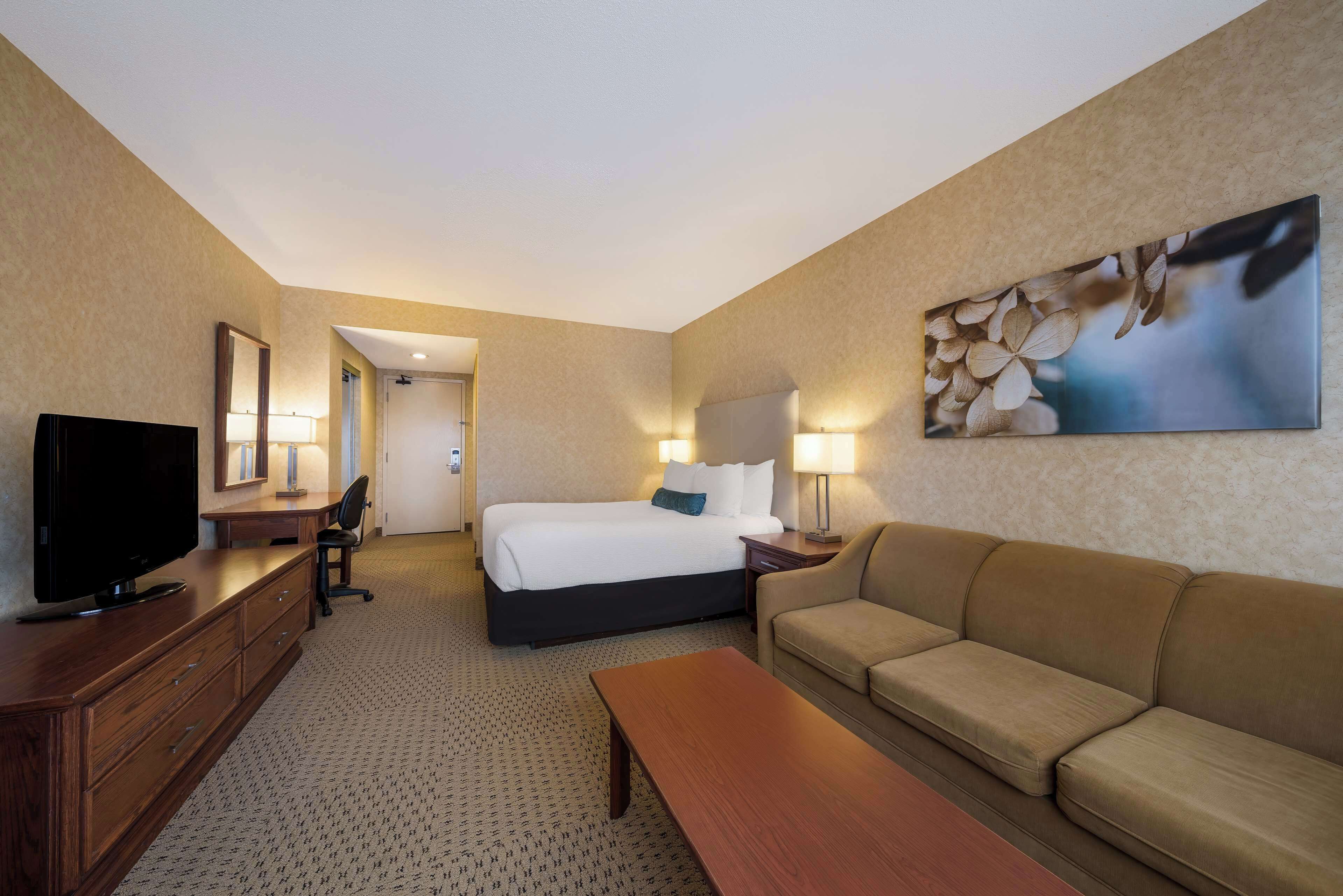 A hotel room with a bed, a sofa, a TV, a desk, and a painting on the wall.