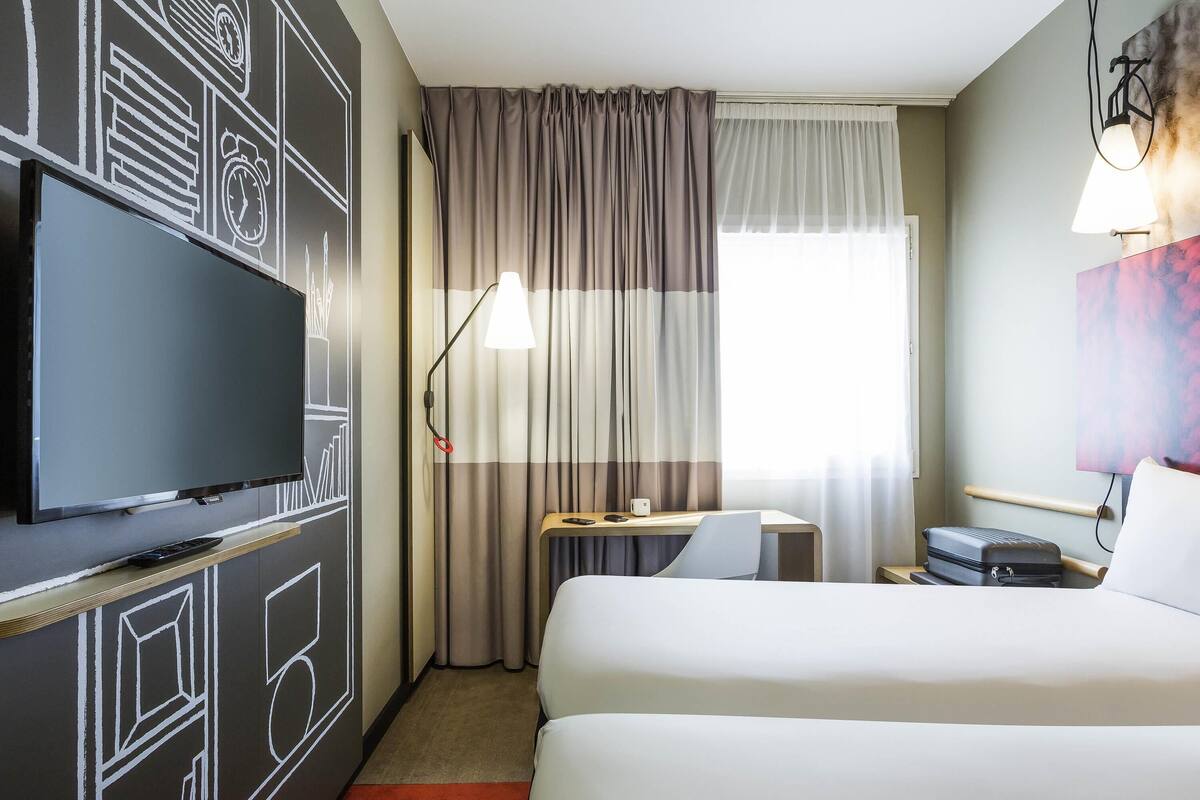 A hotel room with a bed, a desk, a chair, a television, and a window with curtains.