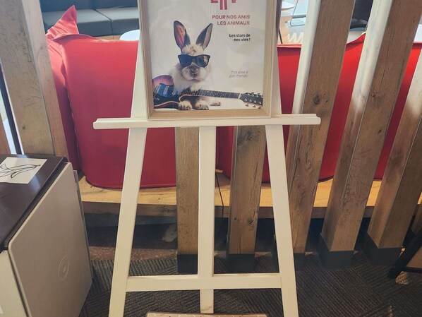 A framed poster with a rabbit wearing sunglasses and a guitar, placed on a white easel in a room with red furniture.