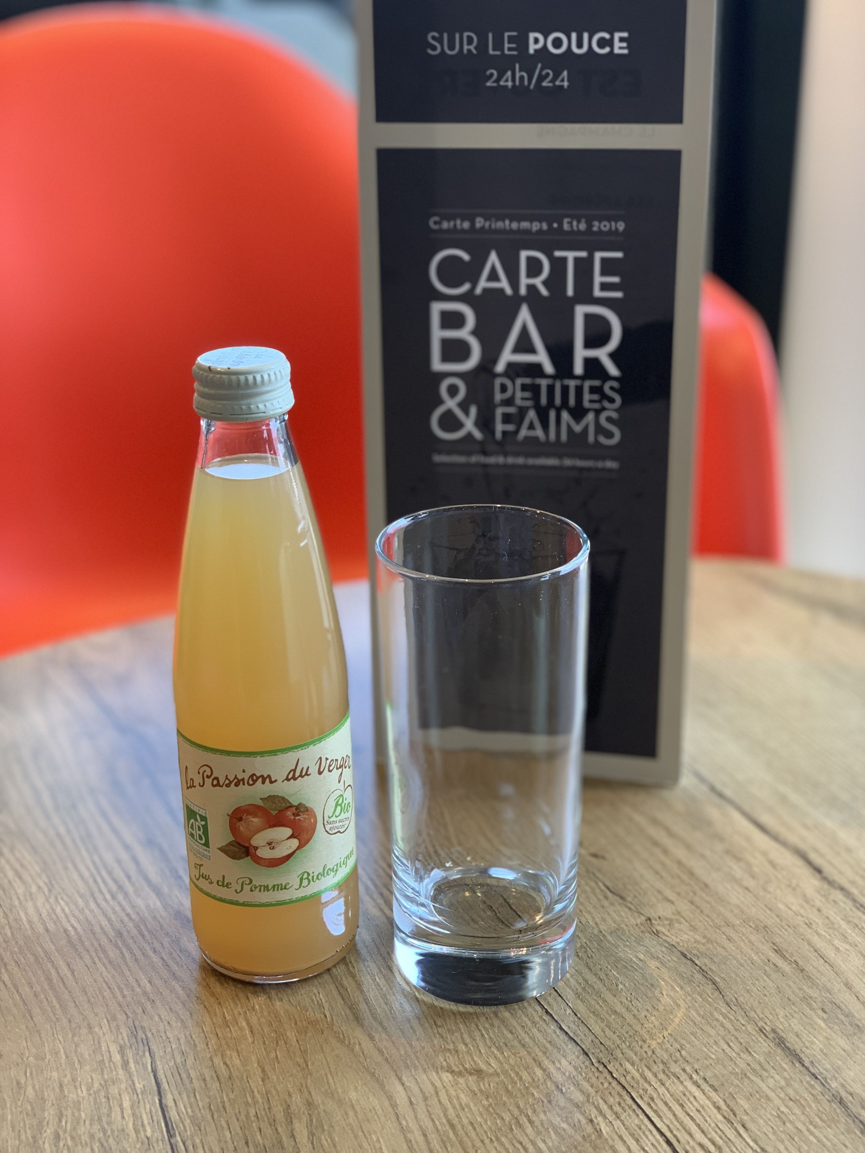 A bottle of La Passion du Verre juice and a glass on a wooden table with a sign in the background.
