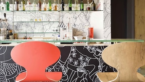 A bar area with shelves of liquor bottles, a red chair, and a wall with black and white abstract designs. - ibis Bordeaux Centre Gare Saint Jean (Bordeaux)