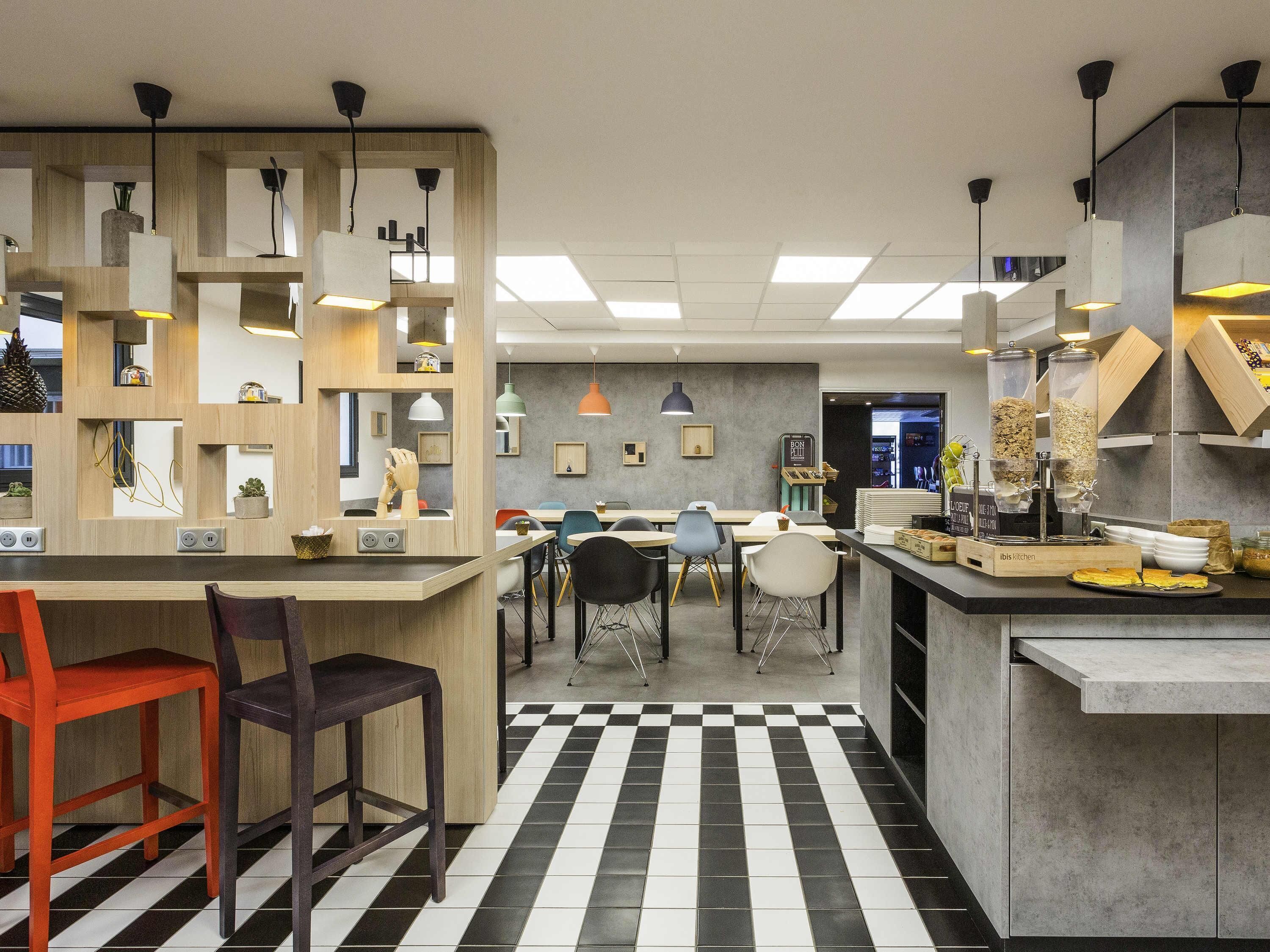 Un café moderno con suelo a cuadros, separadores de madera y diferentes opciones de asientos, incluyendo sillas y un taburete de bar.