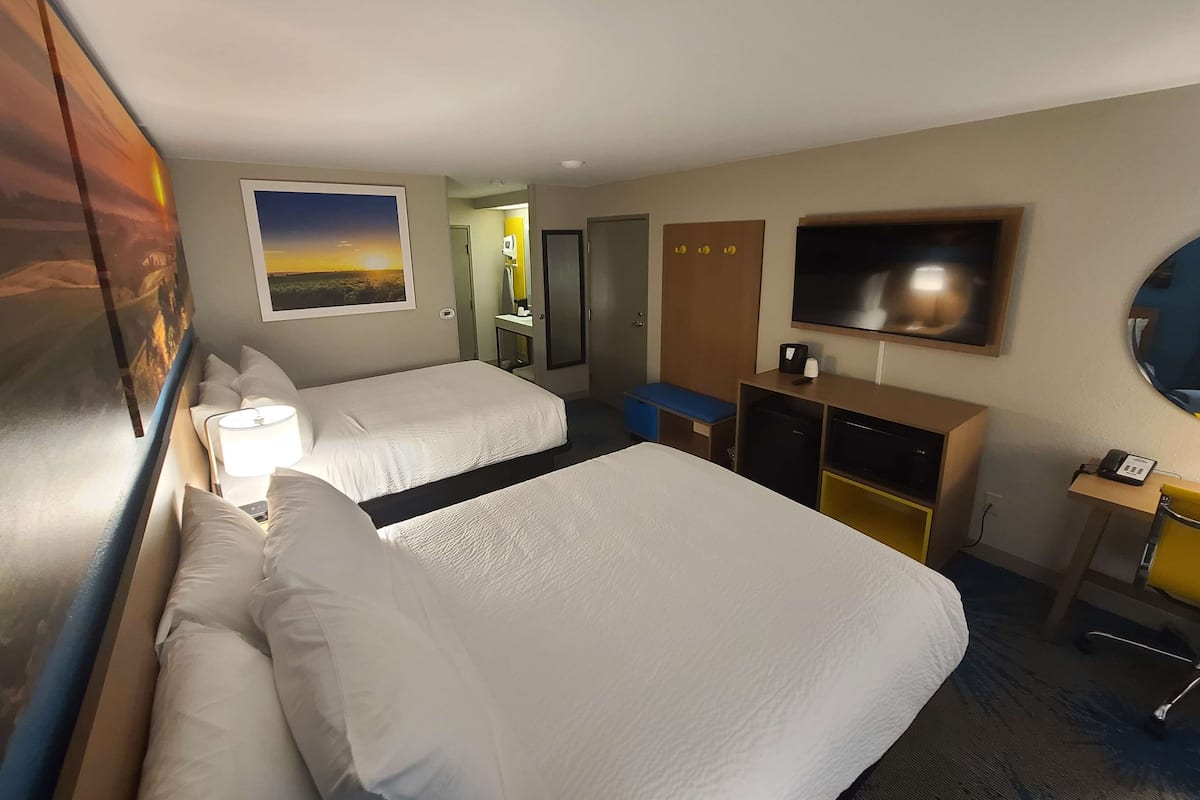 A hotel room with two beds, a desk with a computer, a TV, and a mirror.