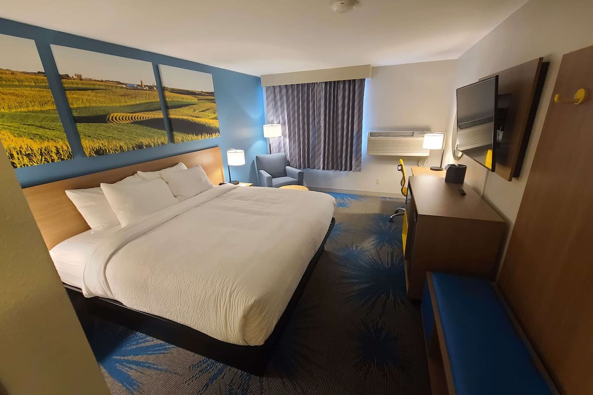 A hotel room with a large bed, a desk with a flat-screen TV, a chair, and a window with curtains.