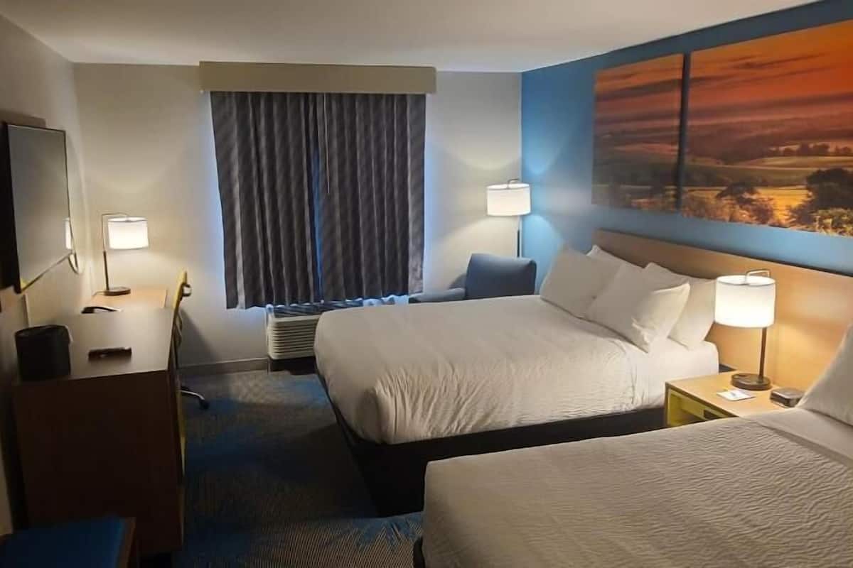 A hotel room with two beds, a desk, a chair, a TV, and a painting on the wall.