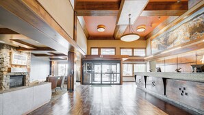 A spacious lobby with a stone fireplace, wooden ceiling beams, and a large reception desk. - Holiday Inn West Yellowstone by IHG. (West Yellowstone)