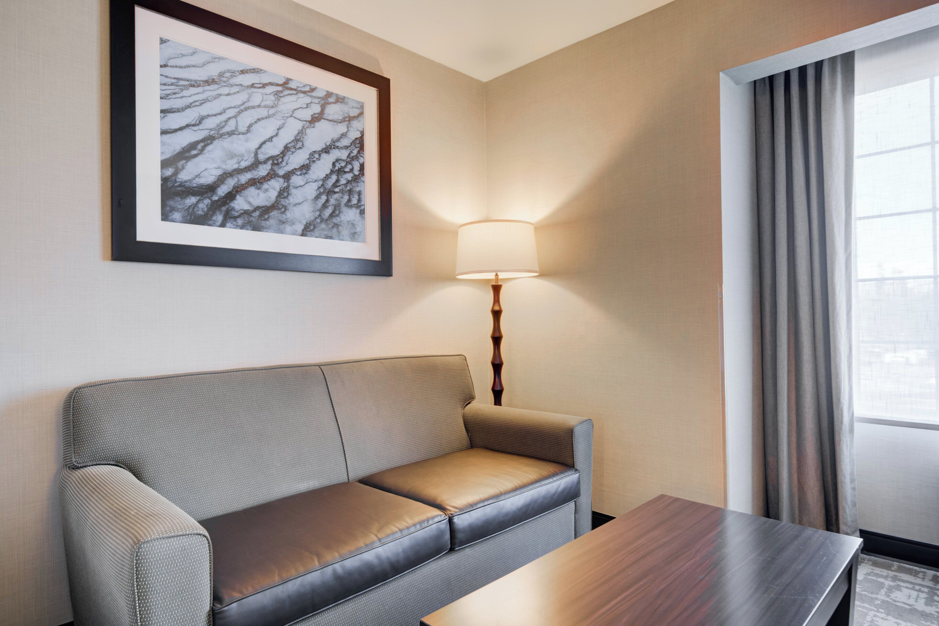 A hotel room with a sofa, a table, a lamp, and a window with curtains.
