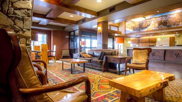 A spacious lobby with a stone wall, wooden furniture, and a colorful patterned carpet. - Holiday Inn West Yellowstone by IHG. (West Yellowstone)