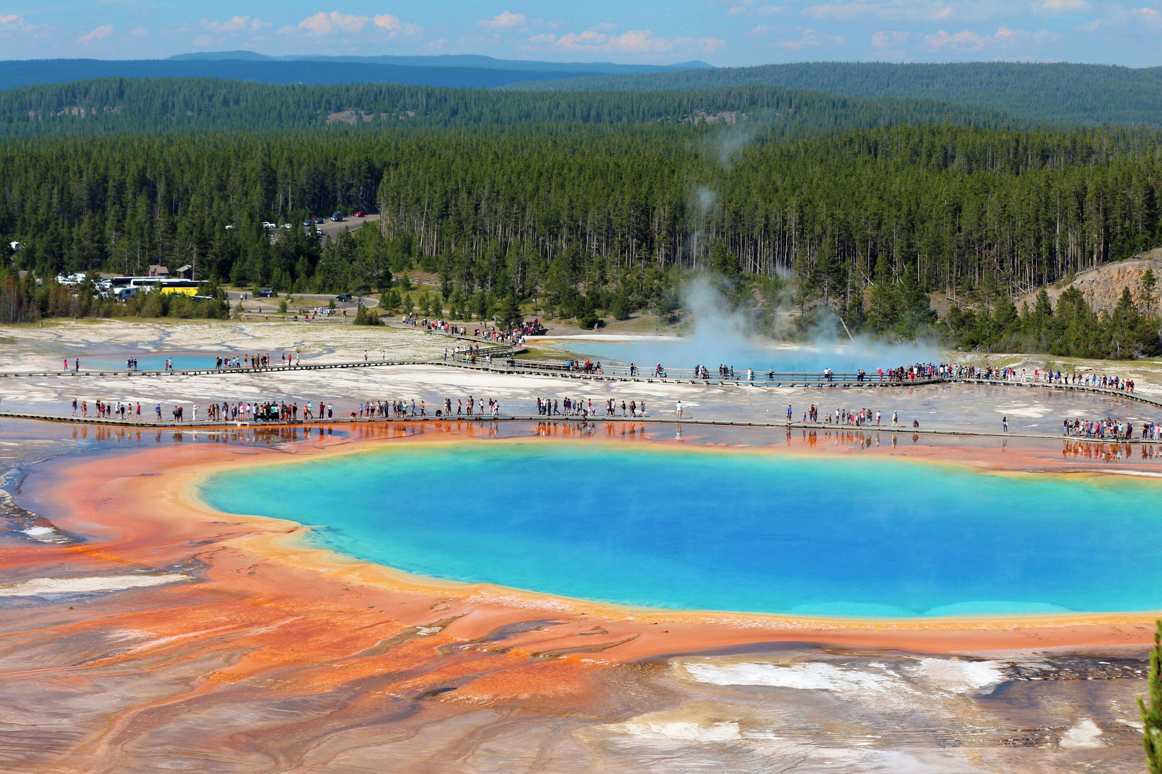 A large natural hot spring with a clear blue center surrounded by orange and red mineral deposits.