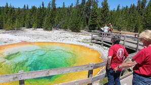 A wooden deck overlooking a geothermal hot spring with a clear view of the surrounding forest. - Holiday Inn West Yellowstone by IHG. (West Yellowstone)