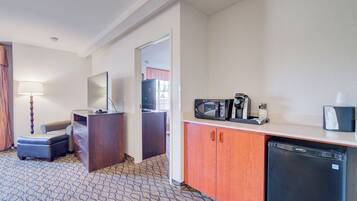 Habitación de hotel compacta con kitchenette, escritorio con lámpara, una silla y un pequeño rincón de estar.