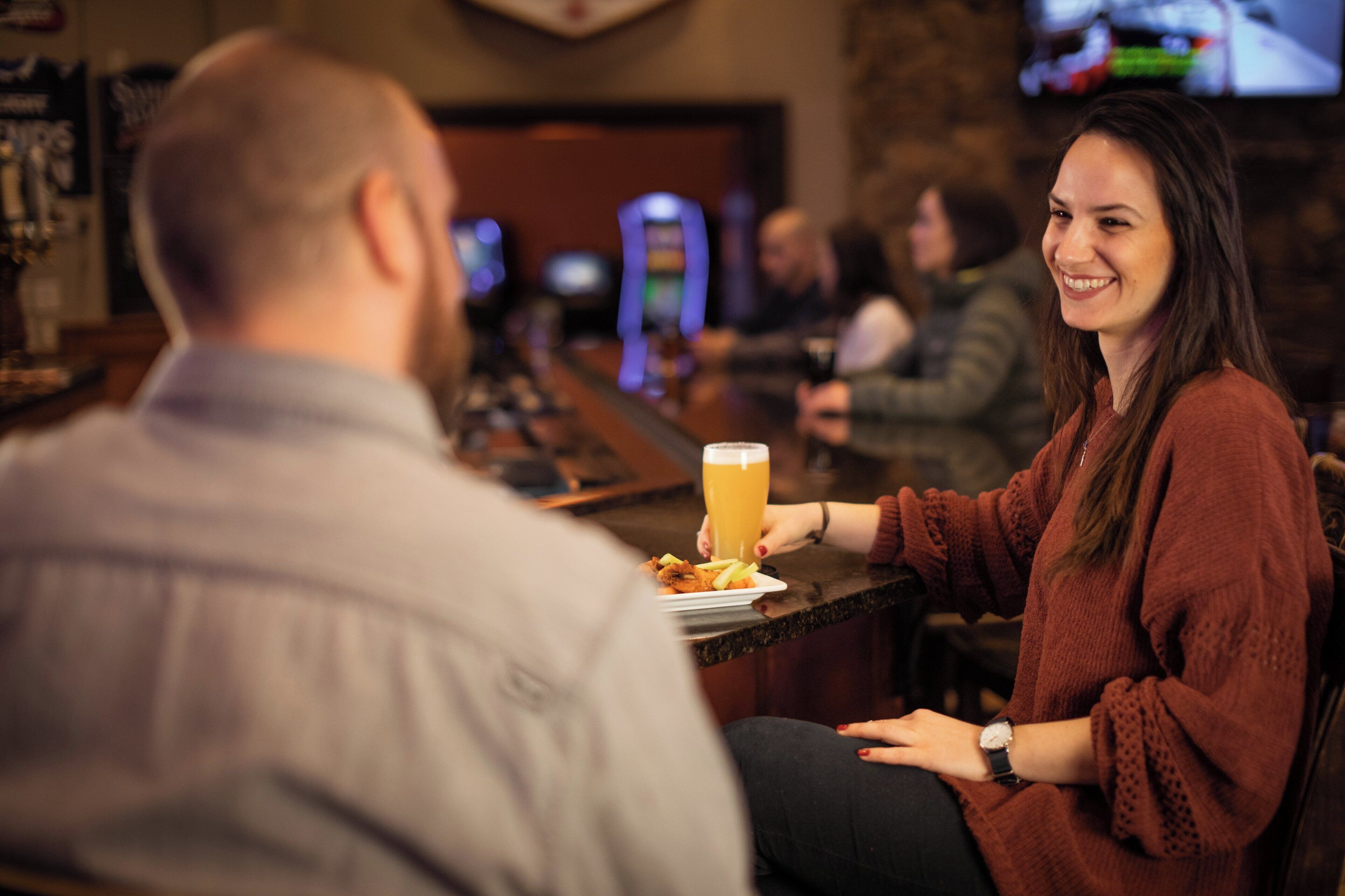 Une scène dans un bar, avec une personne tenant un verre de bière et une autre personne assise en face.