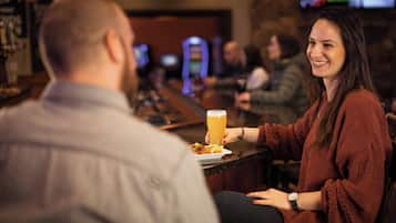 Une scène dans un bar, avec une personne tenant un verre de bière et une autre personne assise en face.