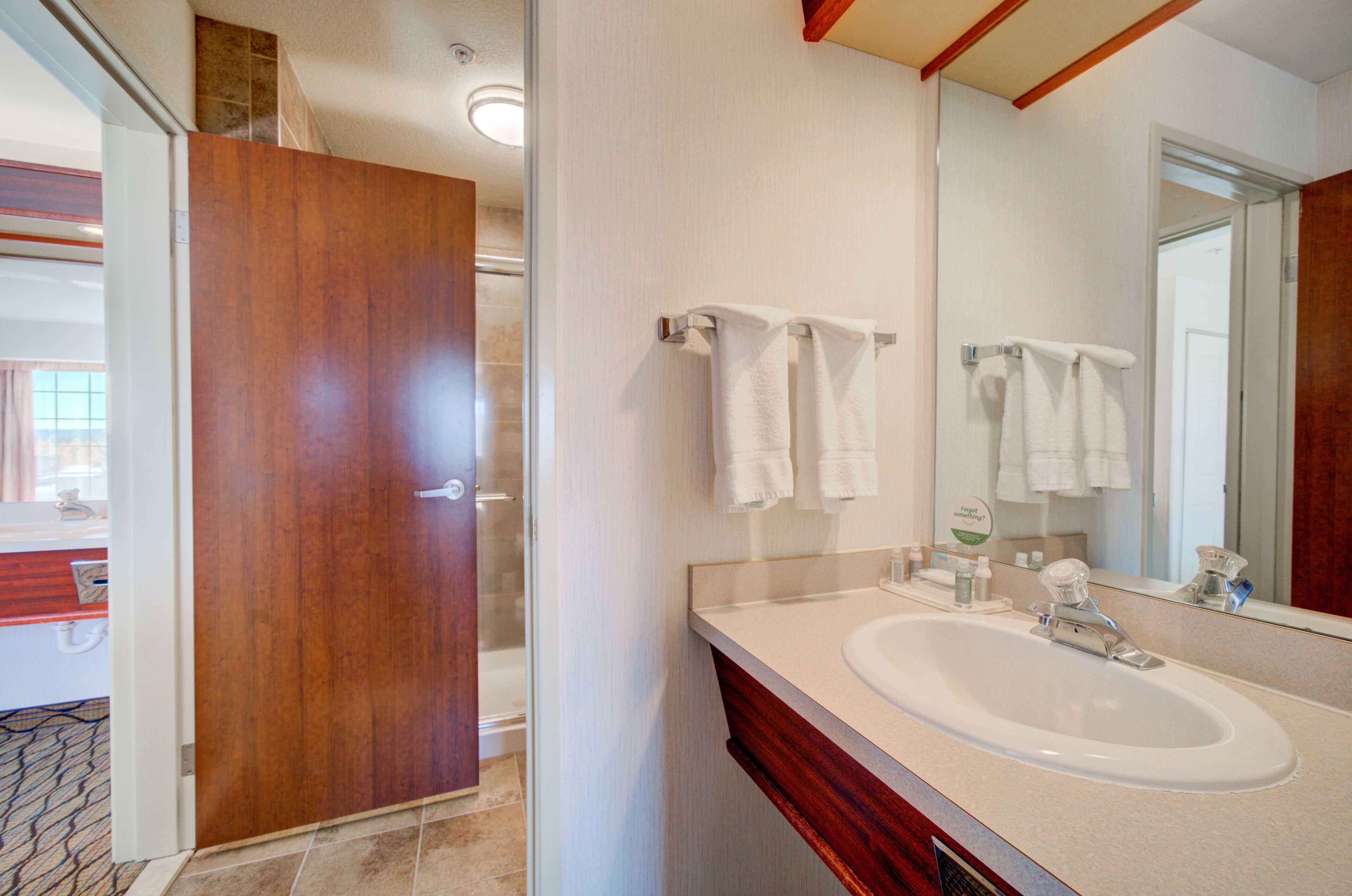 Un bagno con una porta in legno, un lavandino bianco e uno specchio.