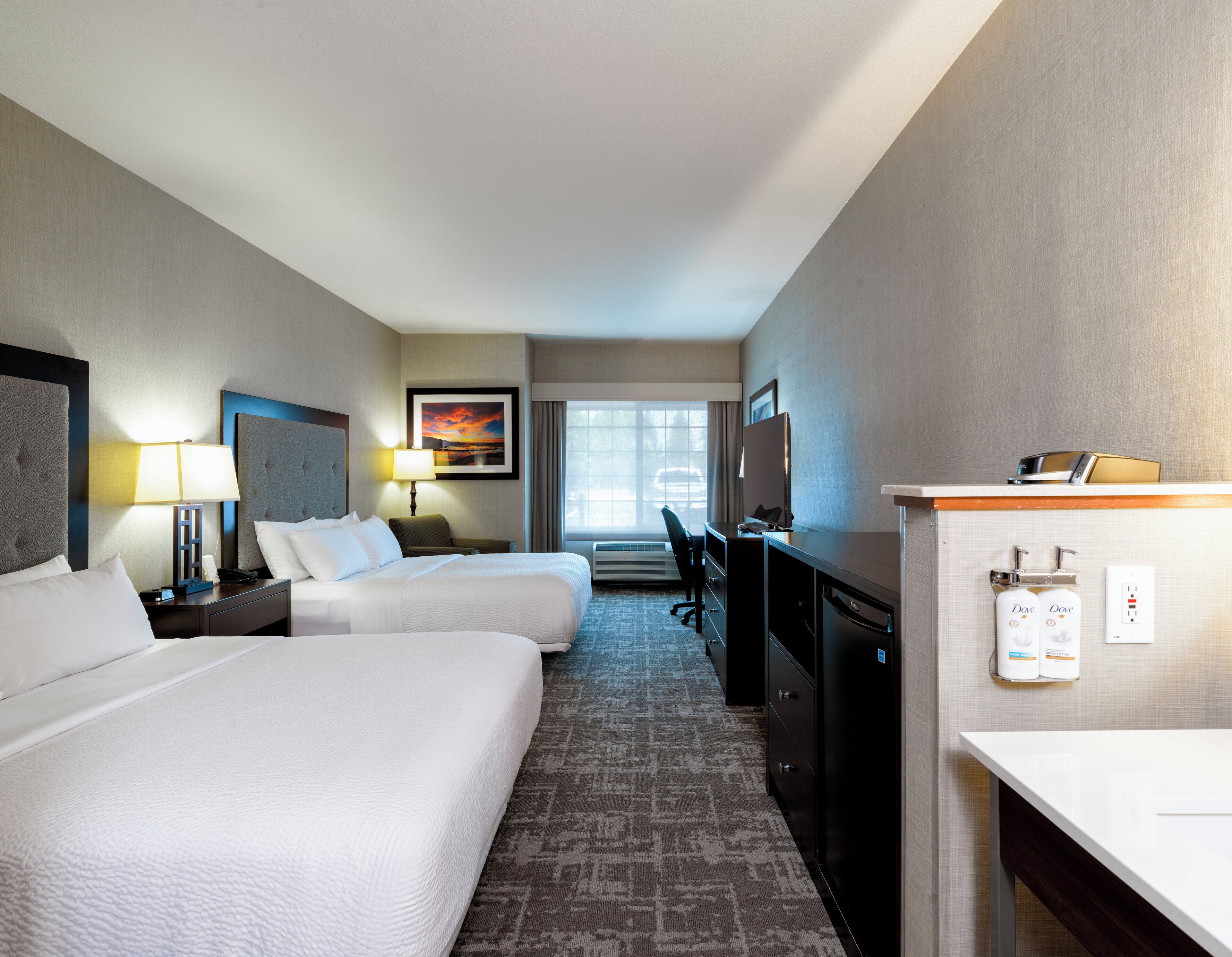 A hotel room with two beds, a desk, a chair, a TV, and a window with a view.