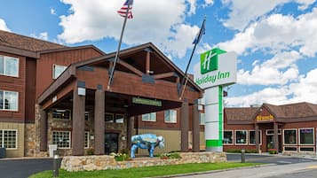 A Holiday Inn with a stone facade, a large American flag, and a unique blue cow sculpture in front.