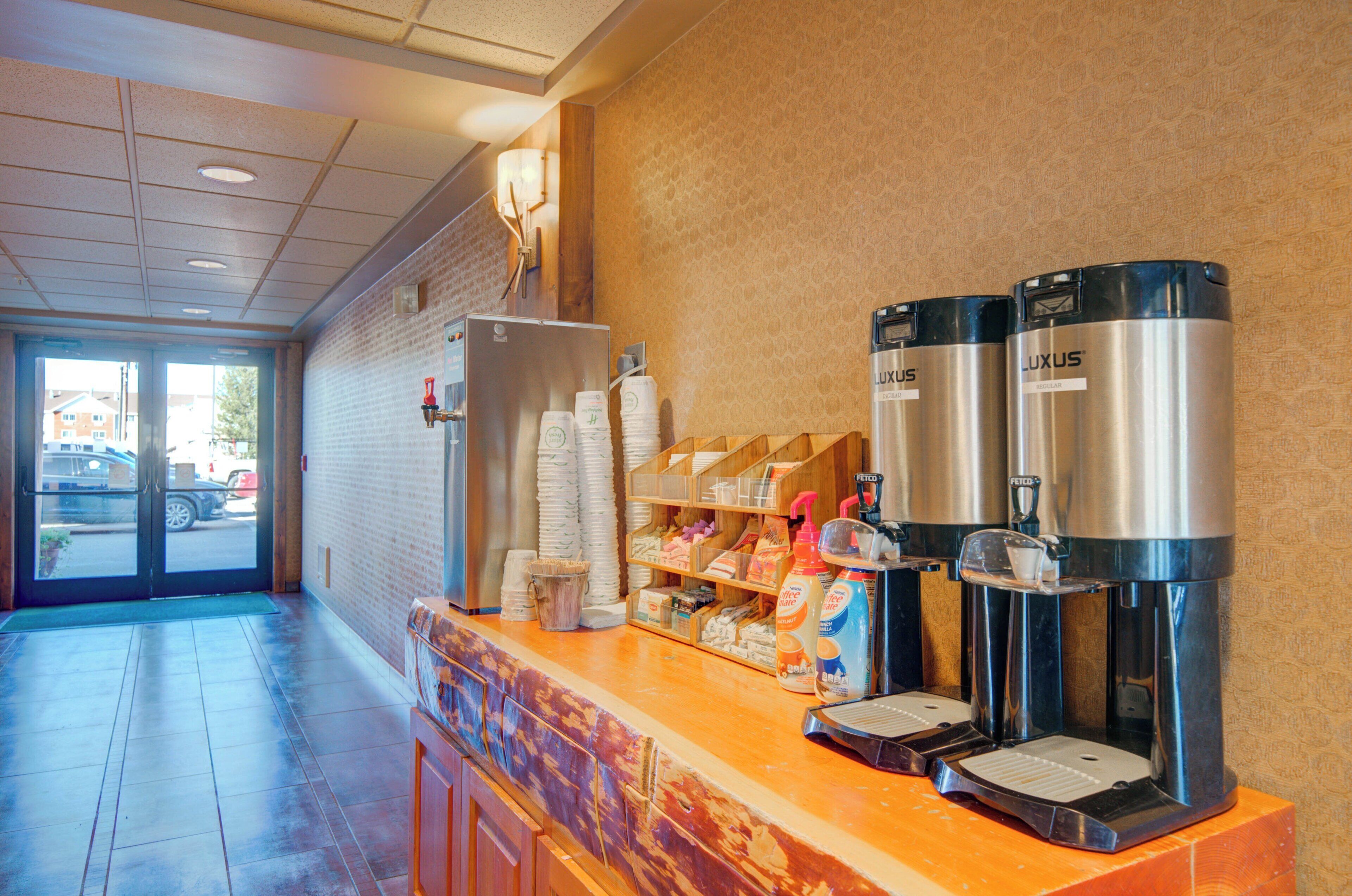 A coffee station with two LUXUS branded coffee machines, a refrigerator, and a variety of coffee pods and supplies.