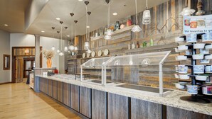 A breakfast bar with a wooden backdrop, clear beverage dispensers, and a variety of breakfast items. - Holiday Inn West Yellowstone by IHG. (West Yellowstone)