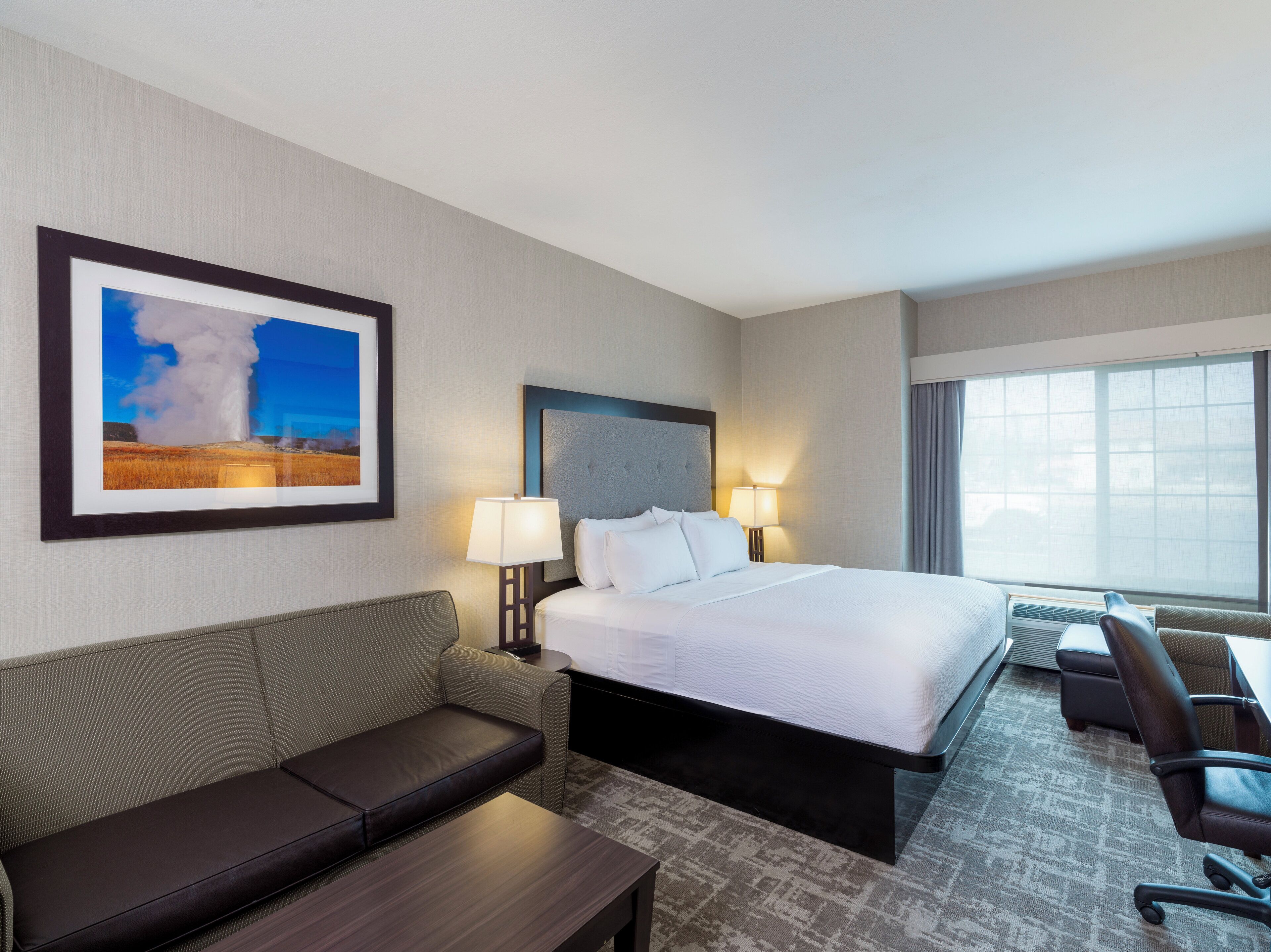 A hotel room with a bed, a sofa, a desk, and a large window.